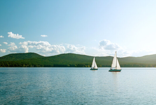Summer vacation background, two white yachts with unidentified people at the lake on the background of the mountains in summer sunny day, summer travel concept