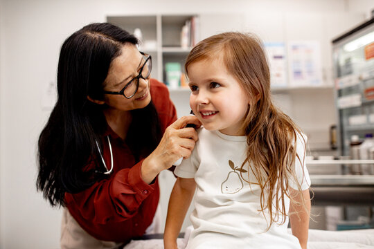 Asian female doctor examining female child&rsquo;s ear with otoscope