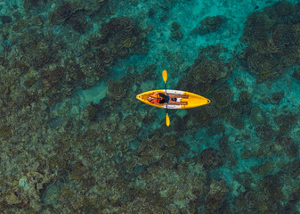 Aerial top view of a woman relaxing on a yellow kayak over a beautiful coral reef in crystal clear turquoise sea water. © SASITHORN