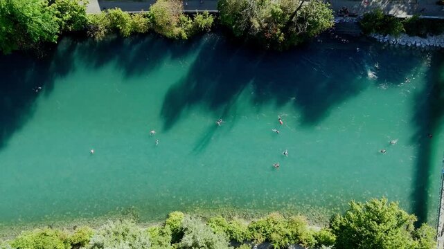 Cinematic drone shot rising slowly over the turquoise Aare river in Bern. Overview of people in colorful inflatable boats and swimmers floating with the current during a beautiful summer day.