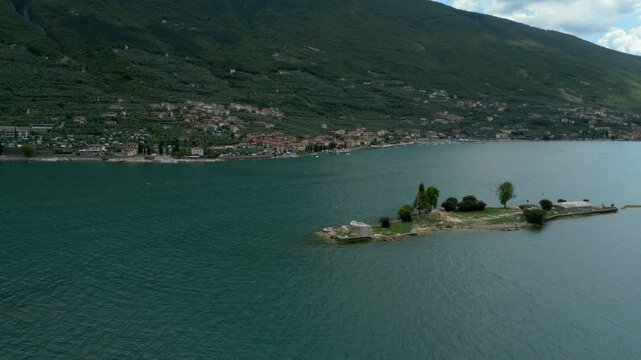 Aerial view passes small Isola del Trimelone with Malcesine and hills in background
