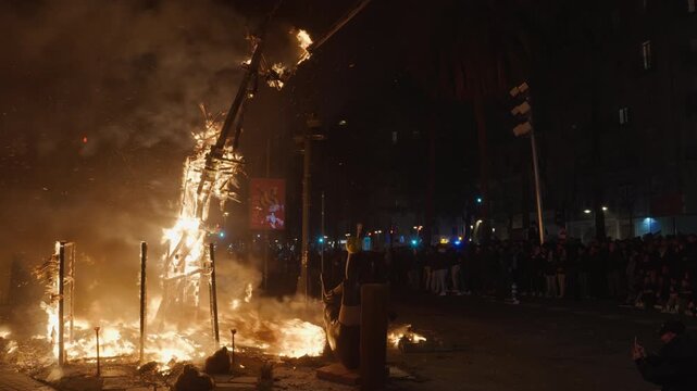 VALENCIA, SPAIN - MARCH 19, 2026: A falla wooden structure collapses in flames during Las Fallas La Crema in Valencia, embers and sparks flying, a dense crowd watching from behind safety barriers