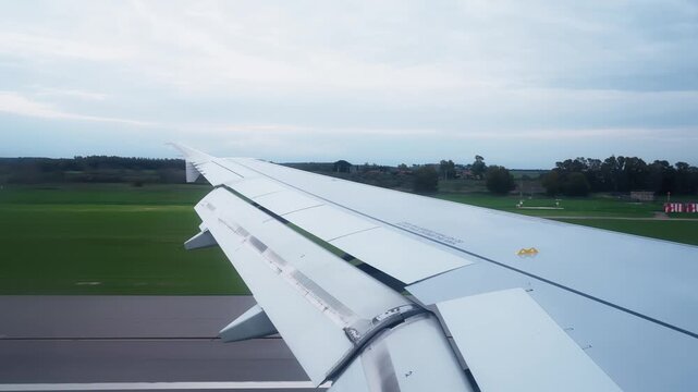 Passenger view over an aircraft wing during landing rollout, with flaps extended above a green airfield and overcast sky capturing a calm arrival moment.