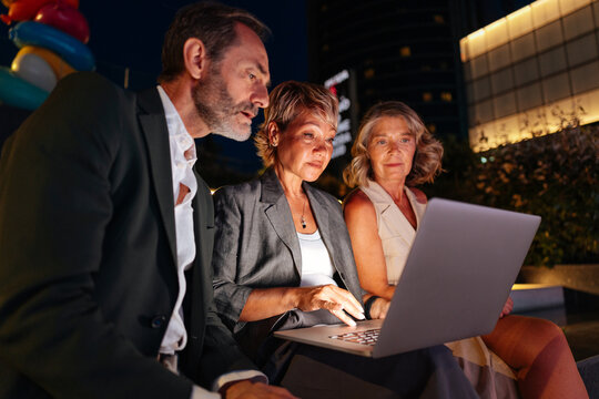Business colleagues collaborating on laptop at city night