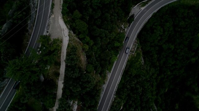 Overhead view as cars drive along winding mountain roads bordered by dense forest