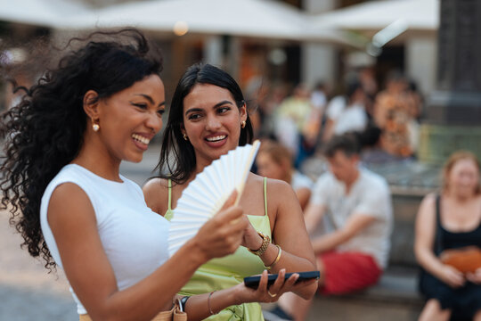 Diverse women friends cooling down with fan on street