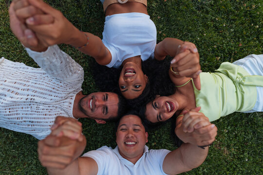 Diverse group of friends lying on grass holding hands