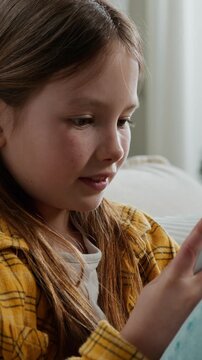 Little teen Caucasian kid girl using mobile phone app smiling satisfied enjoying using smartphone daughter teenager child relaxing at home couch typing message chatting online with cellphone smile