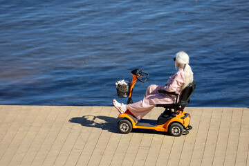 Elderly woman riding electric mobility scooter on a beach. Concept of retirement, wheelchair for mobility aid © Oleg