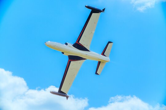 View of a vintage Soko G-2 Galeb jet aircraft performing an aerial display against a bright blue sky with white clouds in Veliki Radinci, Vojvodina, Serbia.