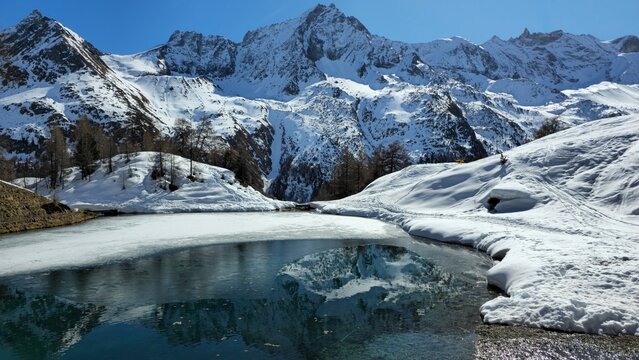 Frozen alpine lake with turquoise water reflecting snow-capped peaks in winter, Lac Bleu d'Arolla, Swiss Alps, Switzerland

