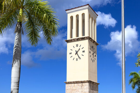 View of the historic yellow clock tower standing tall against a bright blue sky with palm trees in Frederiksted, St. Croix, U.S. Virgin Islands.