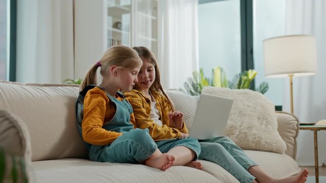 Two little sisters family siblings talking using laptop Caucasian kids daughters girls use computer networks web virtual technology website talk at home relaxing at couch sofa spending time together