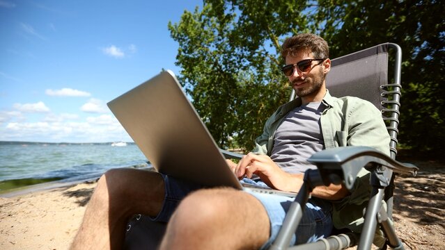 A man is sitting on a beach chair with a laptop in front of him