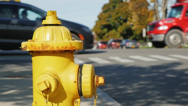 Yellow fire hydrant on city street corner with blurred traffic motion during sunny day.