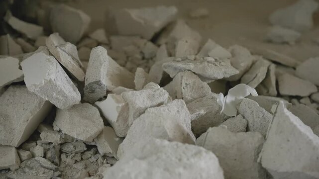 Close up view of broken concrete and plaster debris on dusty floor. Hole in wall from demolition or renovation work. Gritty texture and muted beige tones. Concept of deconstruction or repair