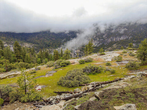 View of the misty valley and distant waterfall surrounded by lush green meadows and pine forests in Yosemite National Park, Fish Camp, California, United States.