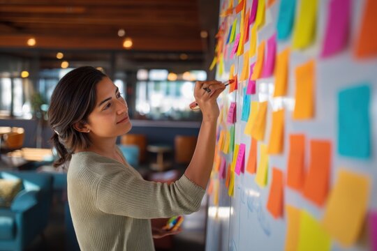 Woman worker placing sticky note on whiteboard in office for project management. Creative professional planning task with post it note. Agile brain storming session for business strategy.