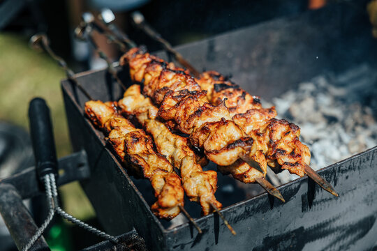 Juicy chicken kebabs roasting on metal skewers over hot charcoal, with charred edges, smoke, and outdoor barbecue atmosphere