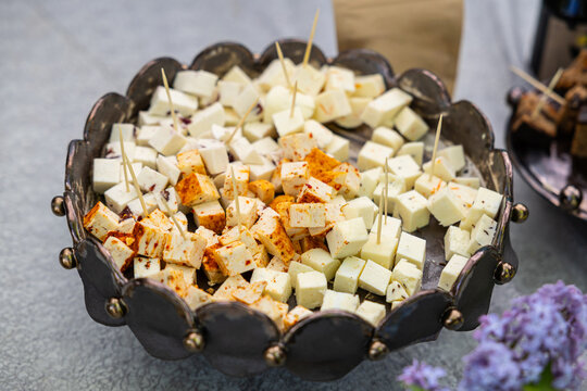Assorted cheese cubes, including seasoned pieces, served with toothpicks in a decorative bowl at a tasting display