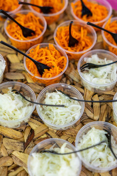 Plastic cups of shredded carrot and cabbage salad with black forks on a woven tray, framed by gray copy space