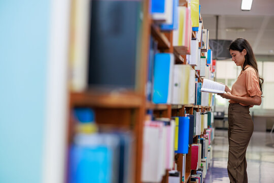 A dedicated female university student reviews academic literature and course materials in a campus library. A concept of higher education, scholarships, and academic success.