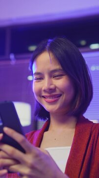 Young Asian woman using smartphone and smiling at mobile screen in home, digital communication and social media concept.
