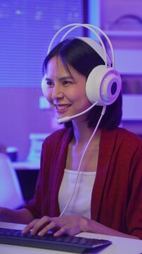 Excited young Asian girl playing online computer game with headset and microphone at home, esports and live streaming concept.