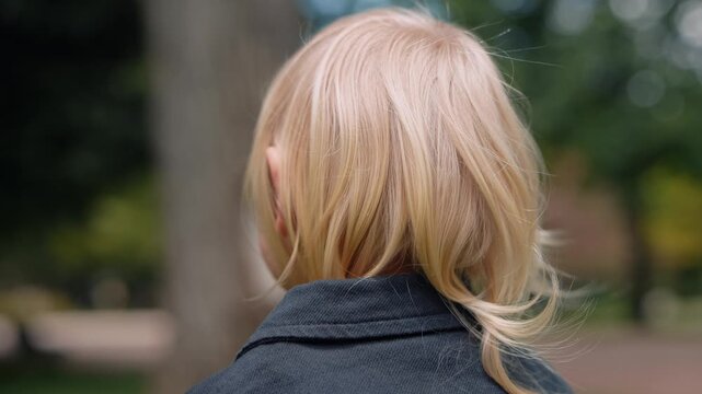 Little blonde girl gazes calmly at park scenes under trees shade