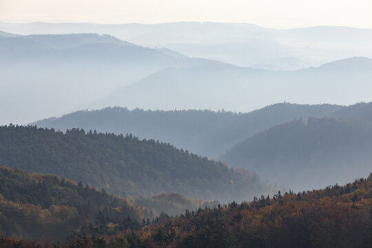 View of the misty Jauerling mountain range with layered forested hills and autumn foliage under a hazy sky in Krems, Niederosterreich, Austria.