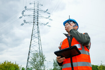 Naklejka premium Technician or inspector evaluating electrical grid infrastructure damage prevention during a pre-storm site survey. Energy engineer speaks on portable radio for real time reporting. 