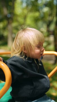 Toddler in summer park playing on spinning device with leaves