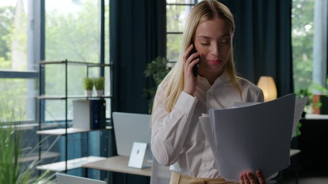 Caucasian businesswoman excited satisfied with documents talking mobile phone business woman communicate call about papers female girl with paperwork feeling carefree joyful happy smiling in office