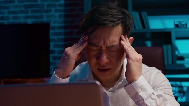 Ill sick unhealthy Asian business man working laptop feeling headache Korean businessman work computer suffering head pain ache Chinese agent tired Japanese male with migraine at night evening office