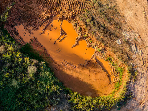 Aerial view of an excavation site featuring a pool of muddy orange water surrounded by cracked earth and green vegetation Coimbra, Coimbra District, Portugal.