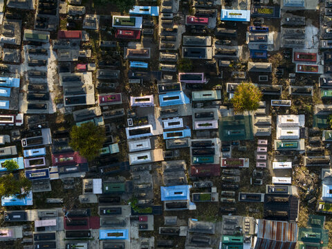 Aerial view of Sasana Laya Gipik Plaosan cemetery with colorful grave markers and scattered trees under warm sunlight Kecamatan Prambanan, Jawa Tengah, Indonesia.