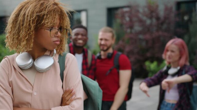 Stressed African American student girl woman suffering with bullying in high school college academy university in city outdoors classmates multiracial students bully mocking laughing discriminate