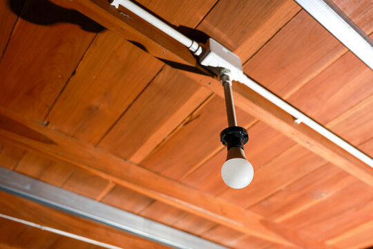 Warm and inviting interior featuring bright light bulb hanging from rustic wood ceiling with visible electrical conduit providing calm illumination for indoor architectural space
