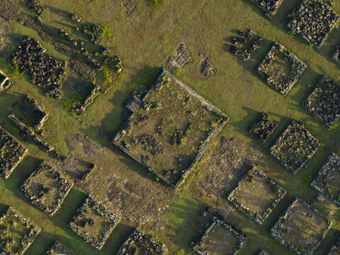 Aerial view of Plaosan Kidul Temple ruins with square stone foundations and scattered ancient blocks on a green grassy field Kecamatan Prambanan, Jawa Tengah, Indonesia.