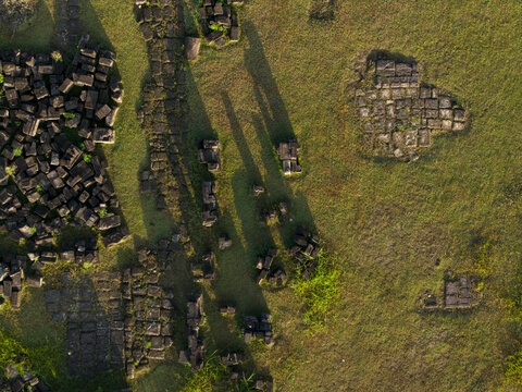 Aerial view of the scattered stone ruins of Plaosan Kidul Temple on a green grassy field with long shadows during golden hour Kecamatan Prambanan, Jawa Tengah, Indonesia.