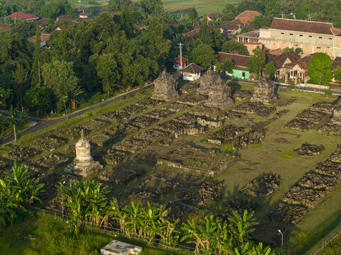 Aerial view of Plaosan Kidul Temple featuring ancient stone ruins, lush green trees, and surrounding village houses in warm light, Kecamatan Prambanan, Jawa Tengah, Indonesia.