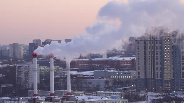 Industrial cooling towers and smokestacks releasing steam with urban residential buildings in the background