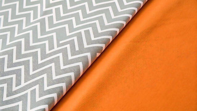 Close up view of folded fabric featuring a gray and white zigzag chevron pattern layered over a solid bright orange textile surface texture