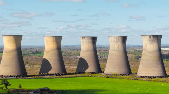 Row of nuclear cooling towers across green fields under cloudy sky, obsolete power generation site. Sustainability issues and environmental impact concept, abandoned industrial structures. Large