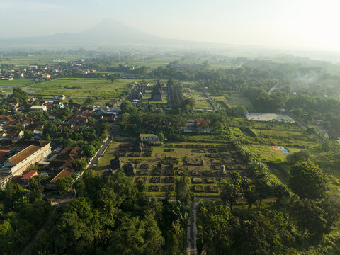 Aerial view of Plaosan Lor Temple complex surrounded by lush green fields and village houses with Mount Merapi in the background Kecamatan Prambanan, Jawa Tengah, Indonesia.