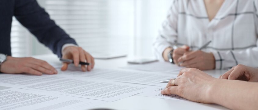 Business people discussing contract documents on a white desk, analyzing clauses and terms during an office meeting, collaborating on important paperwork for agreement