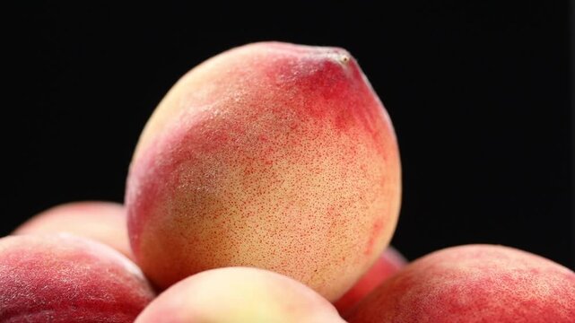 Close-up of a slowly rotating pile of whole fresh peaches on a black background.