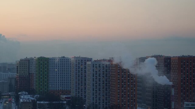 Urban residential district with high-rise buildings and rising steam from chimneys at sunset in atmospheric cityscape