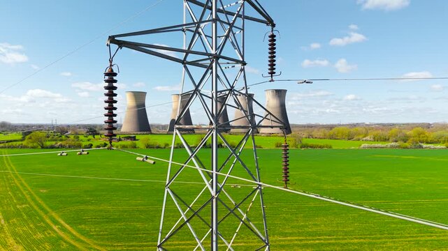 Close angle of high voltage tower structure with wires and insulators against nuclear plant towers. Electrical transmission equipment with industrial energy background and open field. Power grid and