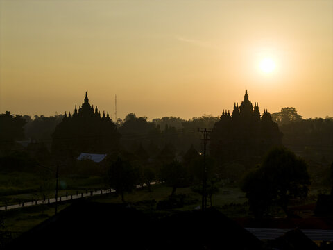 Aerial view of the silhouette of Plaosan Lor Temple during a golden sunrise with misty trees in the background in Kecamatan Prambanan, Jawa Tengah, Indonesia.